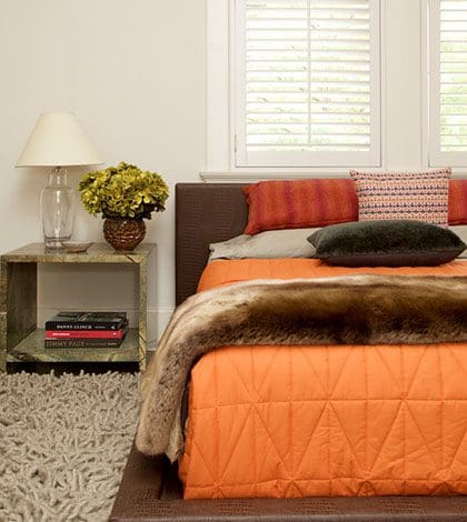 A bedroom with orange and brown bedding, white walls.