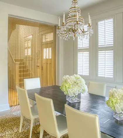 A dining room table with white chairs and a chandelier.