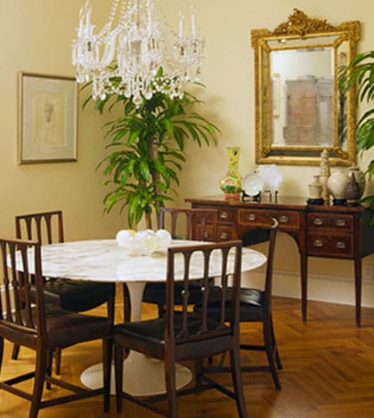 A dining room with a table and chairs, a mirror and a plant.