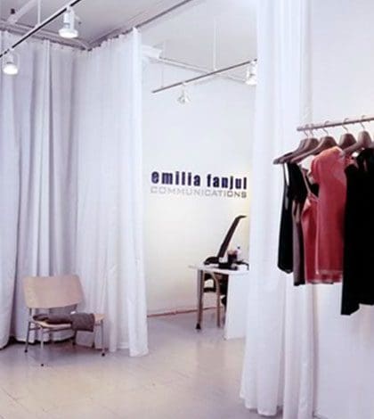 A room with several white curtains and clothes hanging.